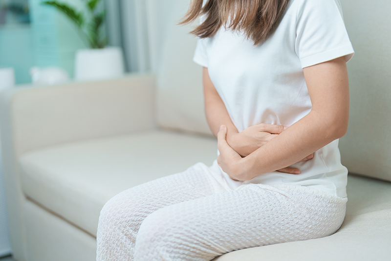 Woman sitting and pressing her hands against her lower belly, showing she’s experiencing abdominal pain or discomfort.
